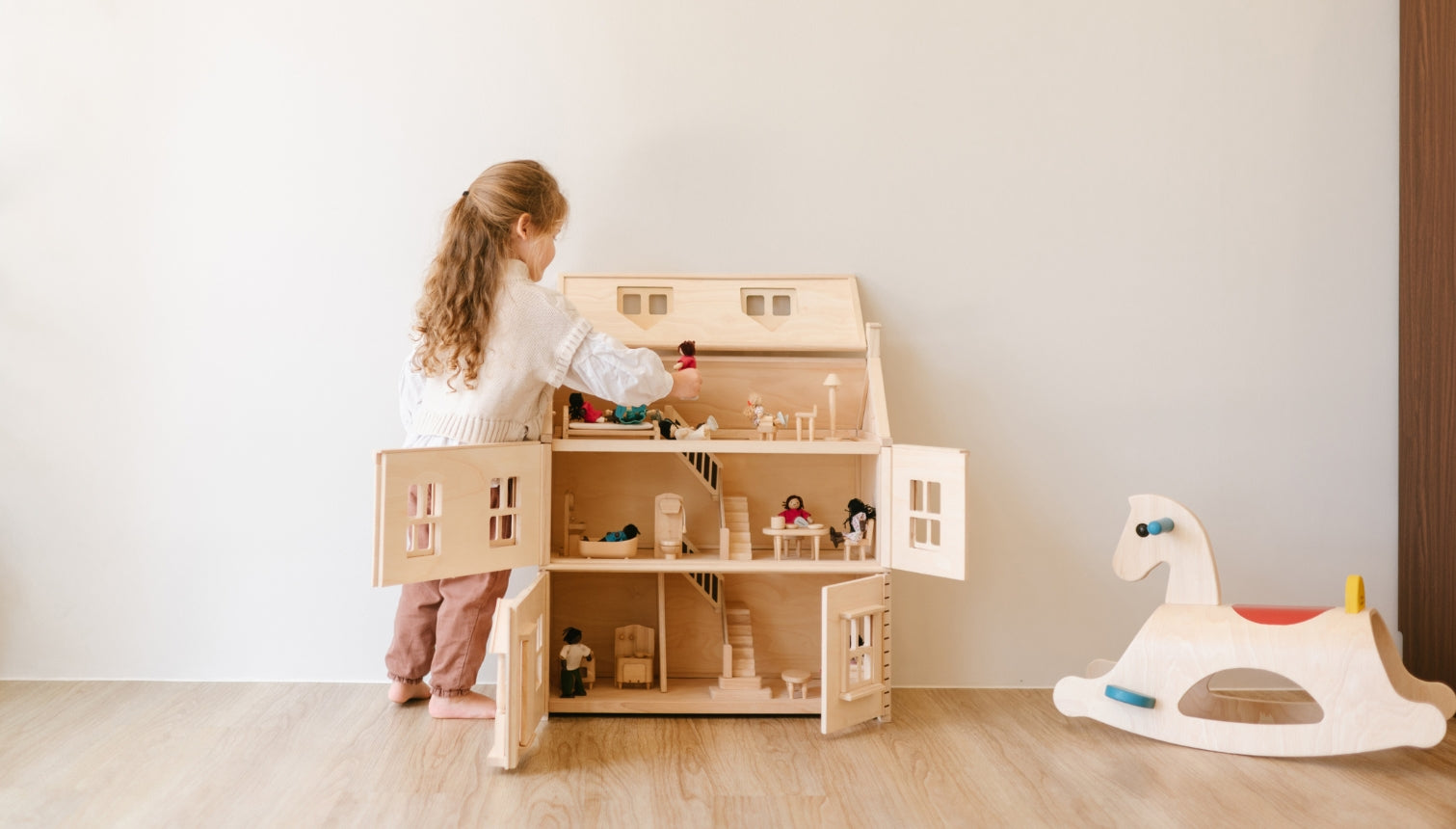 Child playing with a PlanToys wooden dollhouse in a minimalistic room.